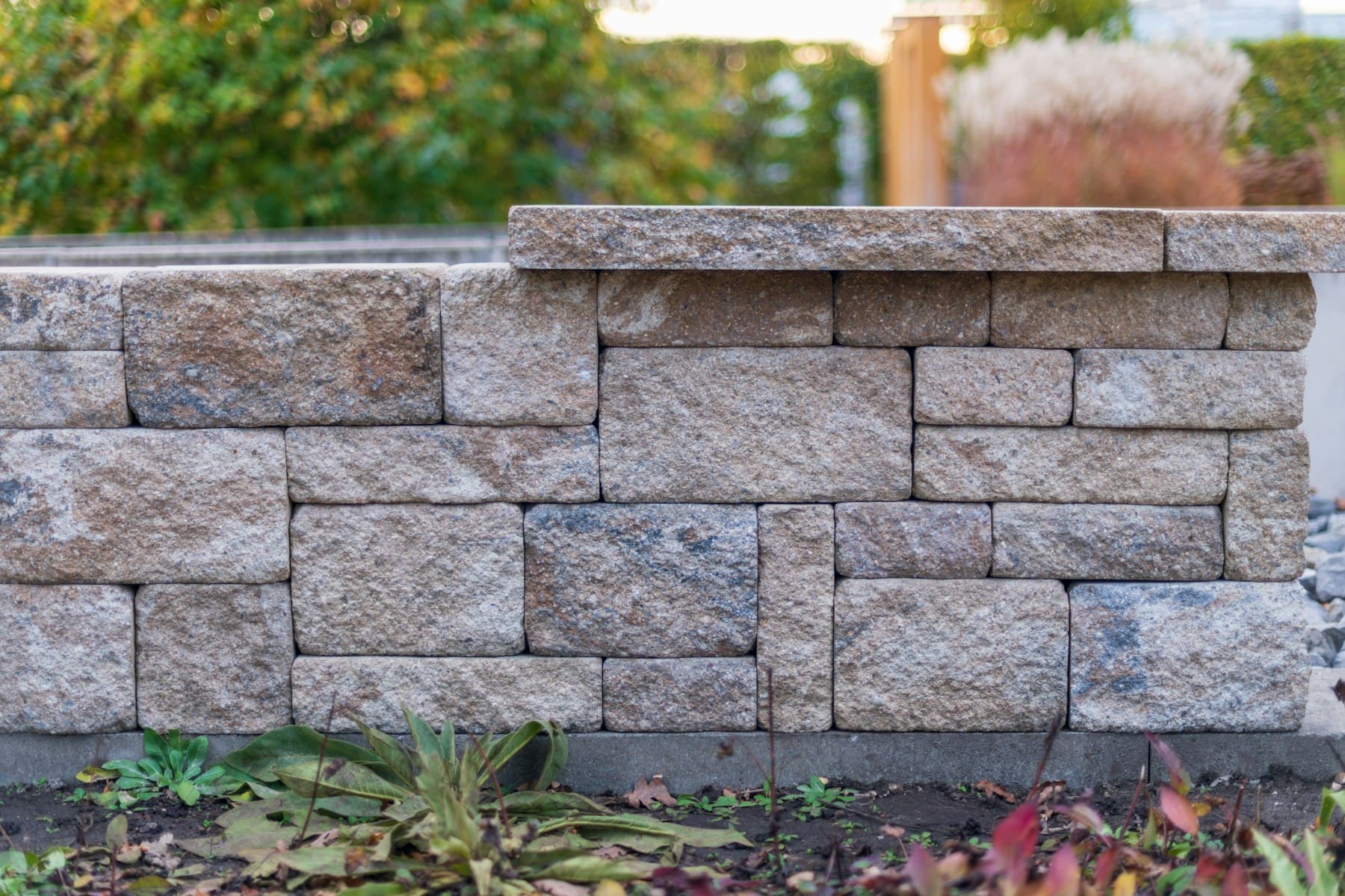 Finished segmental block retaining wall with capstones, photographed in warm evening light against a garden backdrop