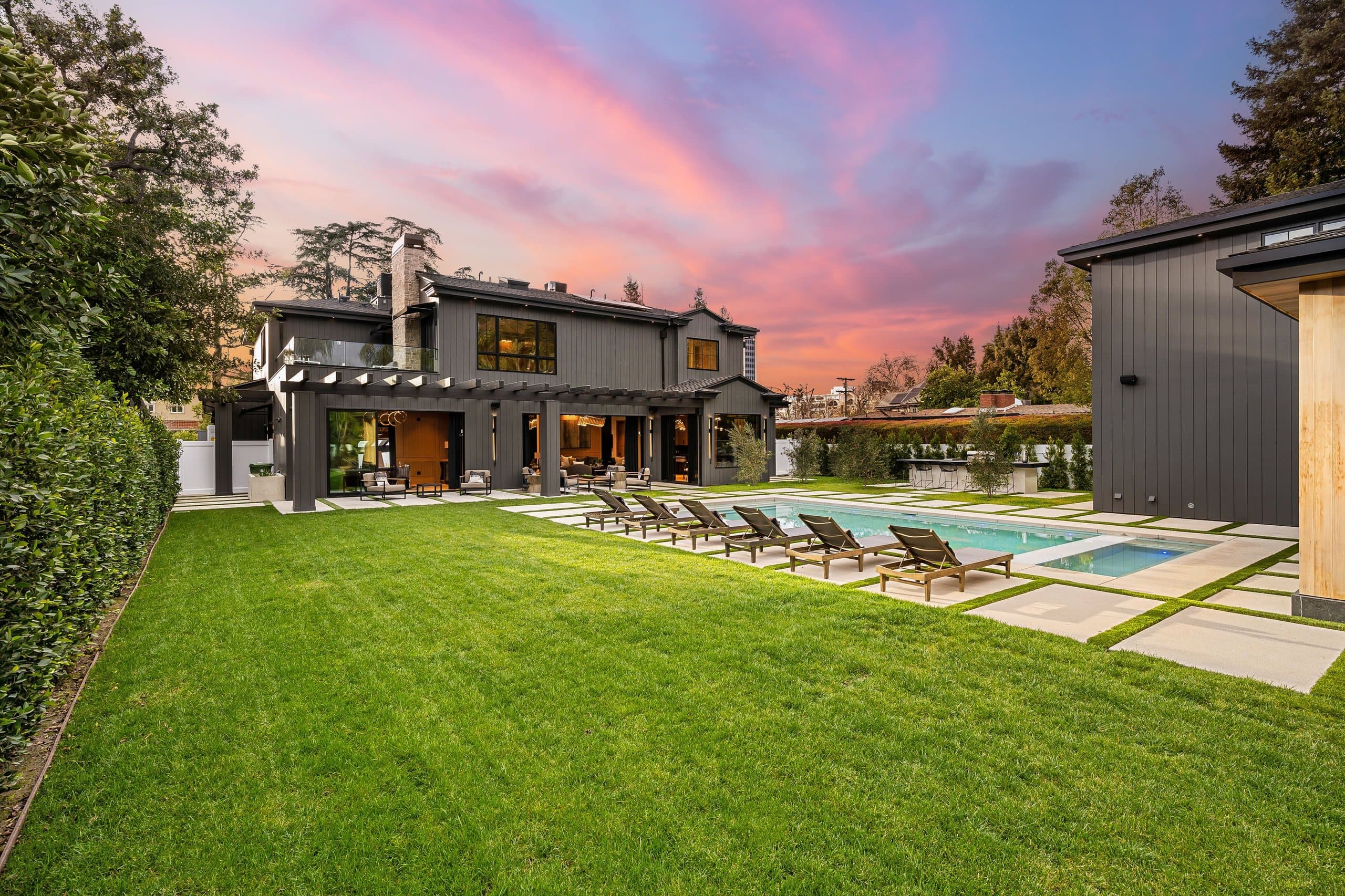 Broad backyard lawn with pool, loungers, and covered patio at dusk — design inspiration