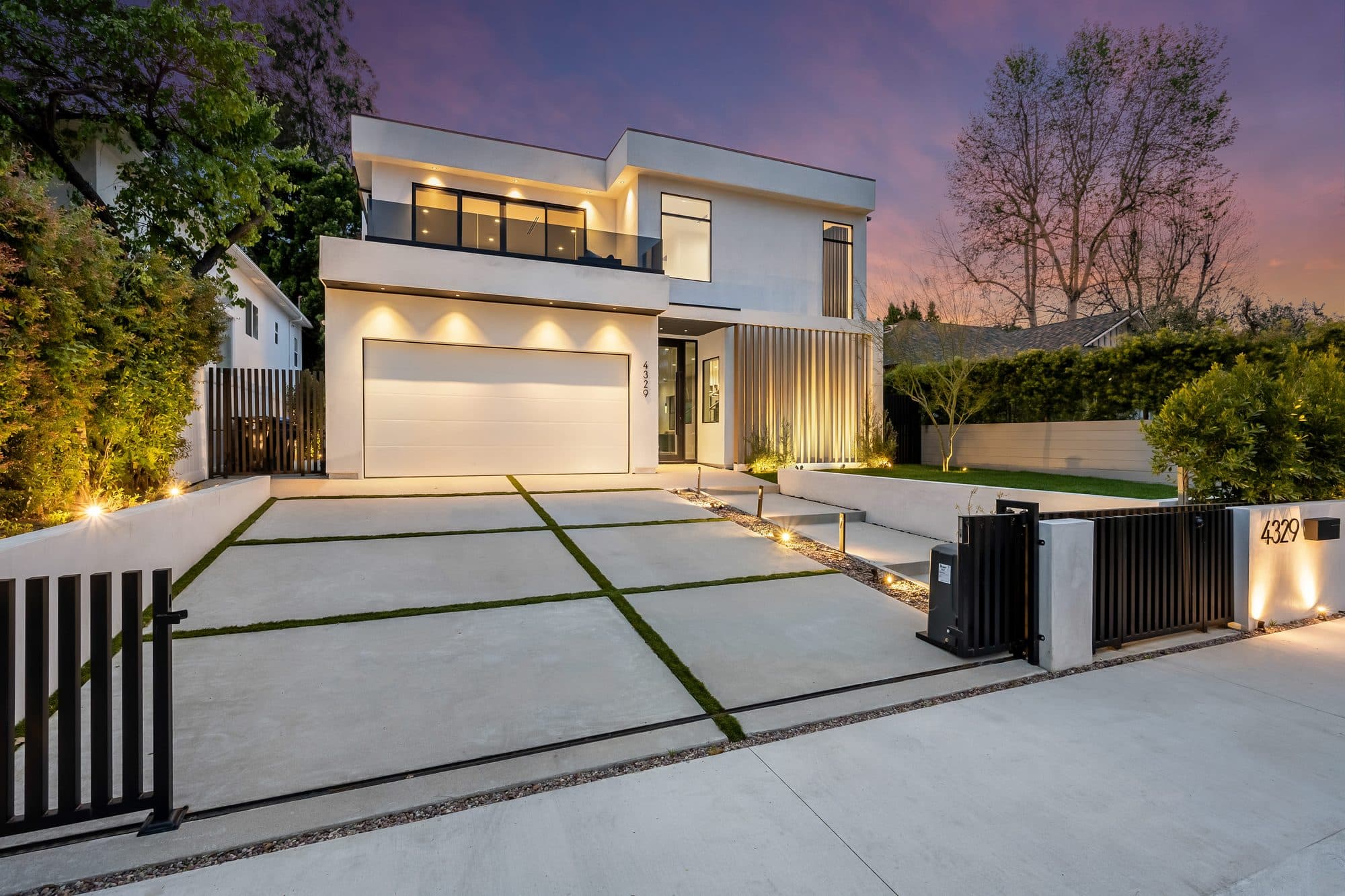 Modern gated home with large concrete driveway slabs separated by turf joints and path lighting