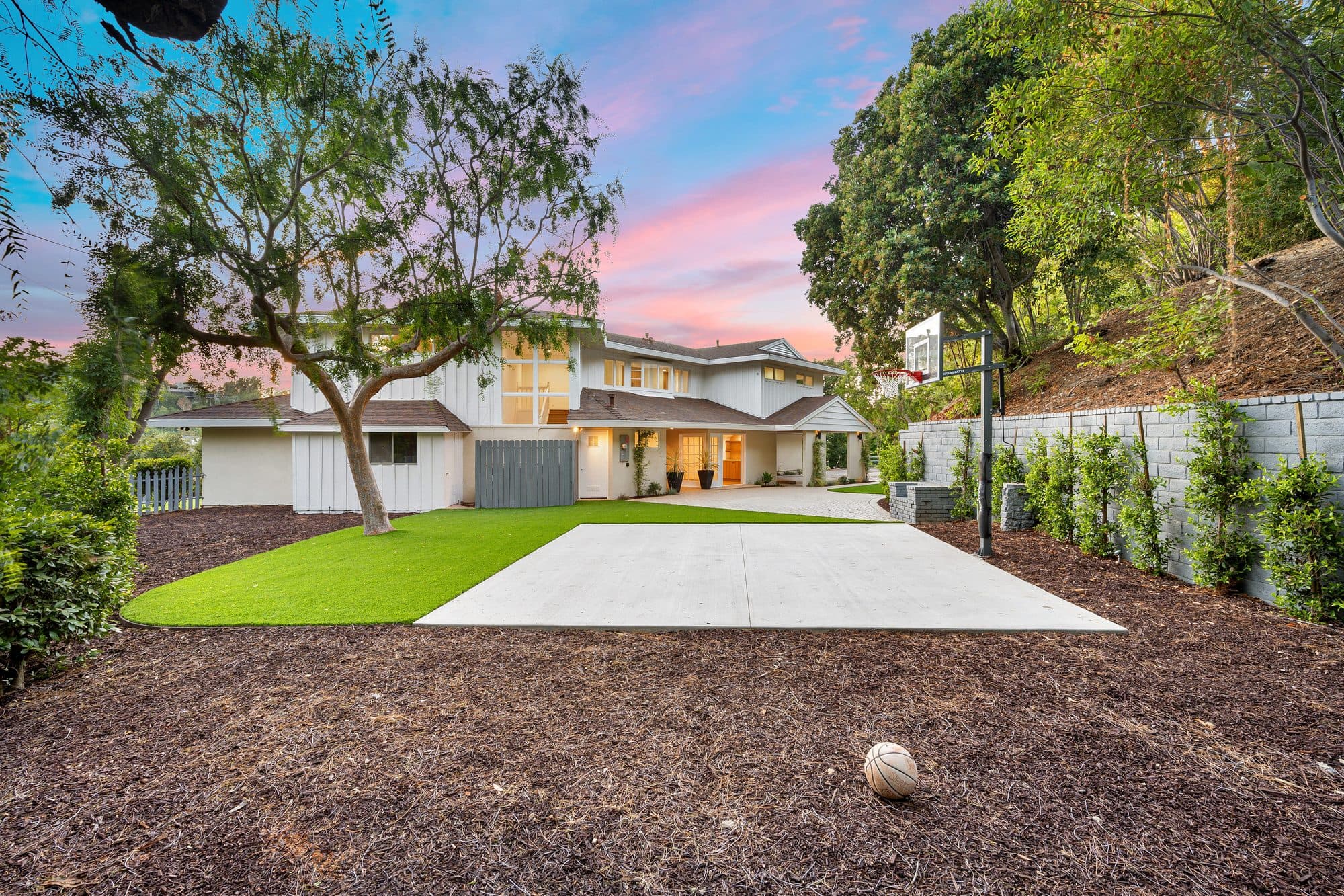 White farmhouse backyard with artificial turf, a concrete sport pad, and fresh mulch beds