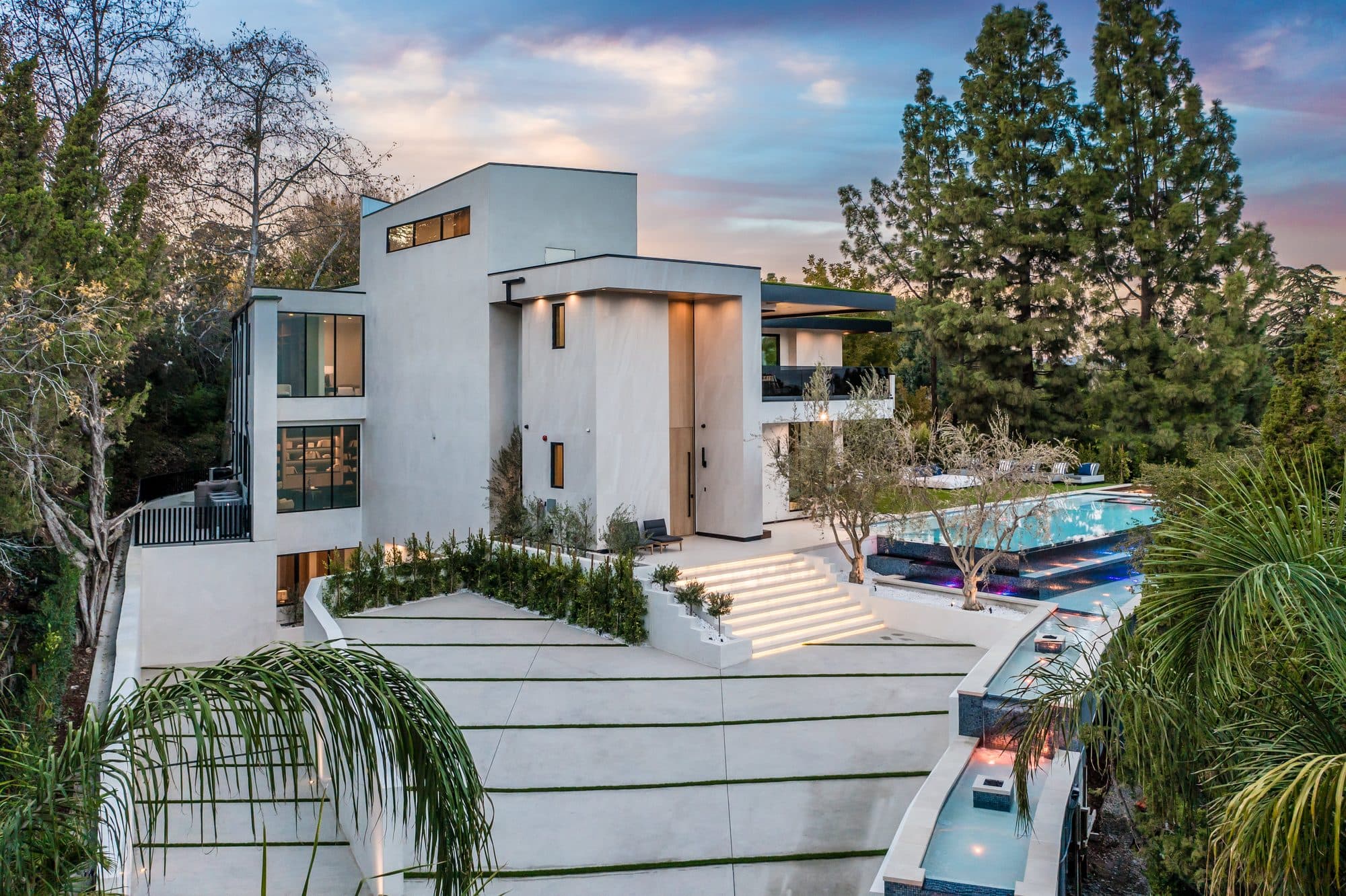 Modern white home with terraced concrete steps and pool at dusk