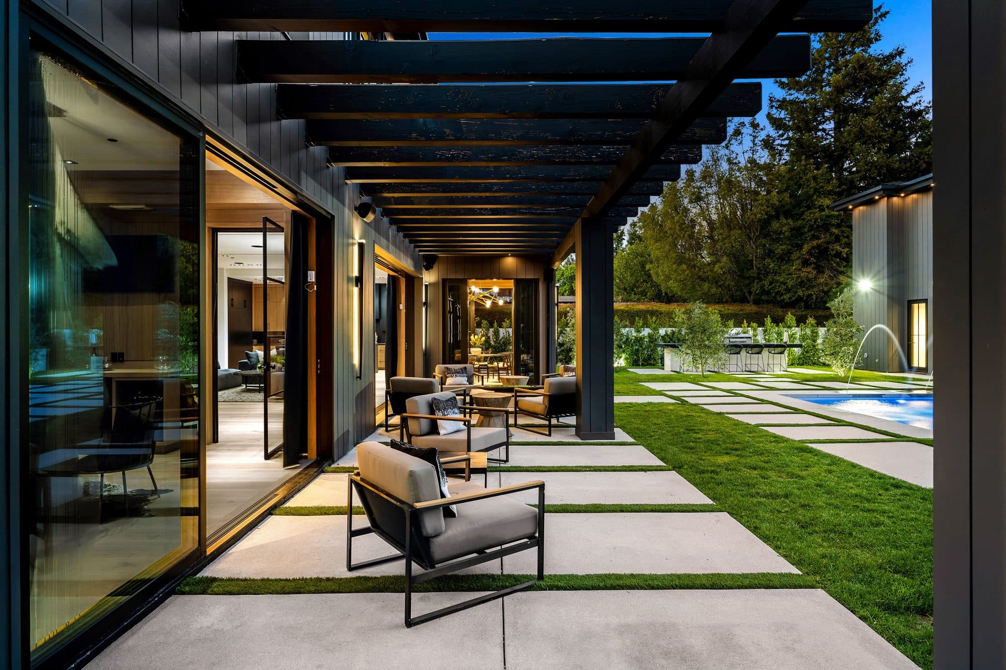 Covered patio with a dark pergola, large concrete slabs with turf joints, and a pool beyond