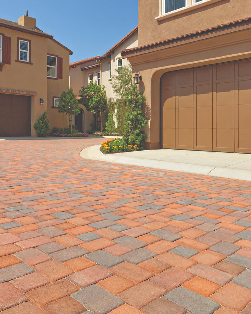 Terracotta-toned antique cobble paver driveway between Mediterranean homes