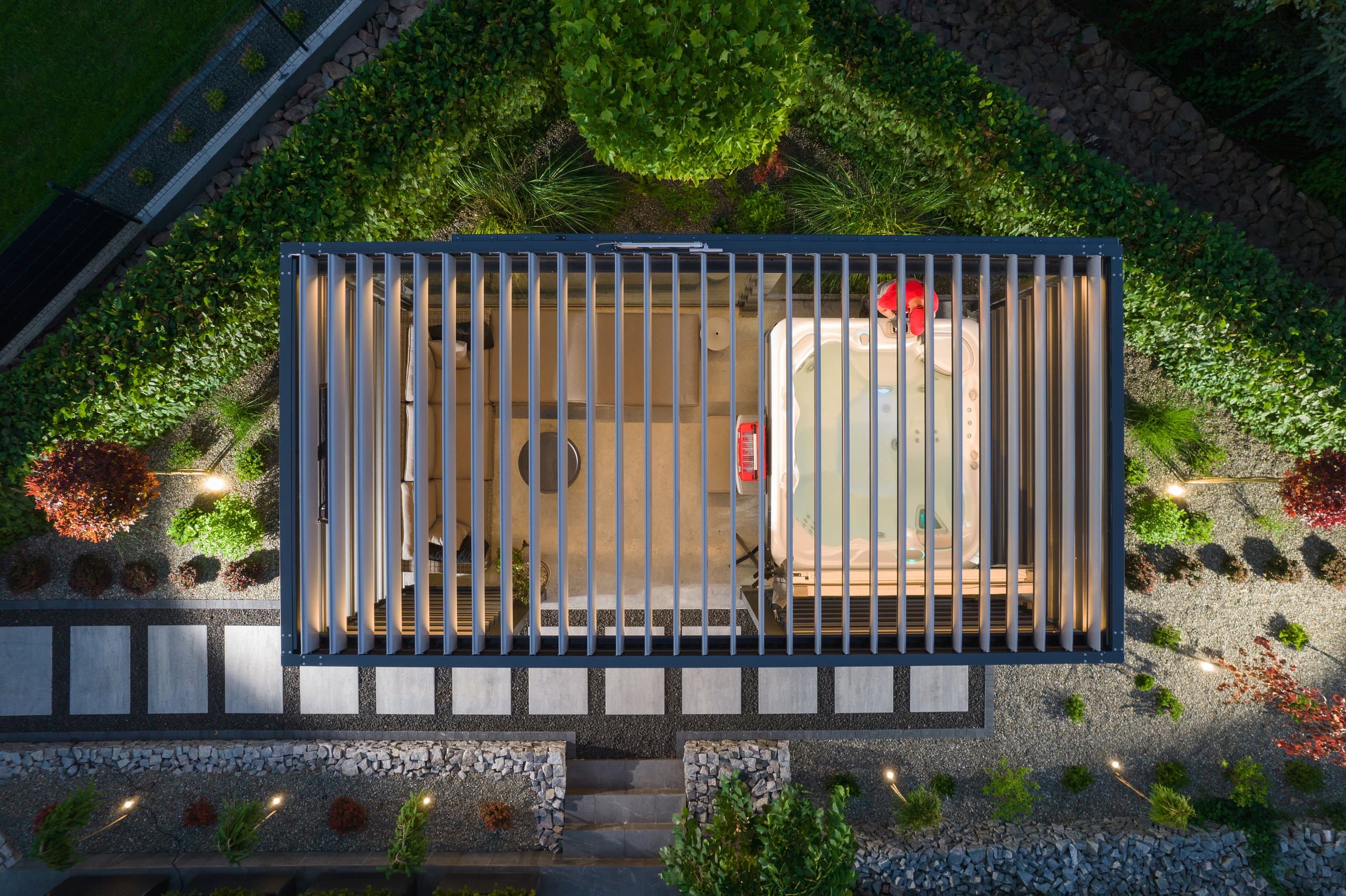 Aerial view of a louvered aluminum pergola sheltering a hot tub and lounge at night