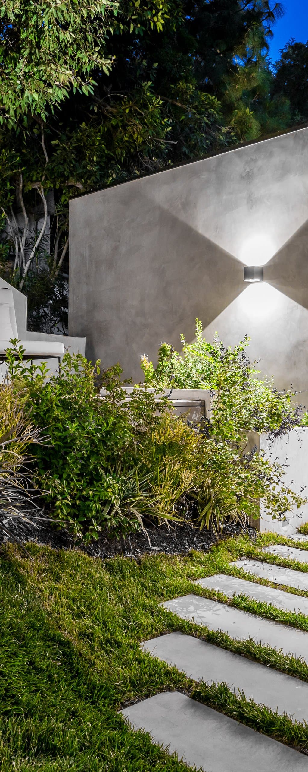 Lit concrete walkway with repeating ornamental grasses and path lights at dusk