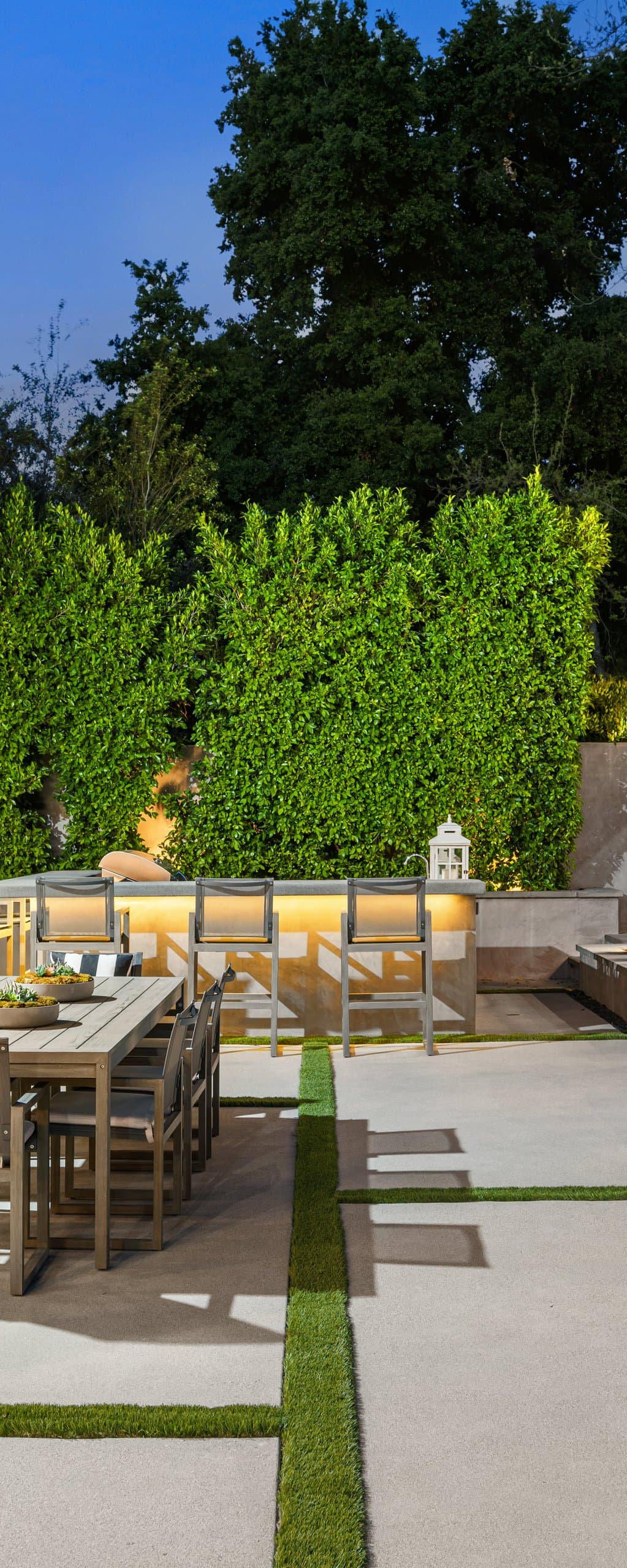 Symmetric grid of concrete pavers and clipped topiary spheres in a formal garden at dusk