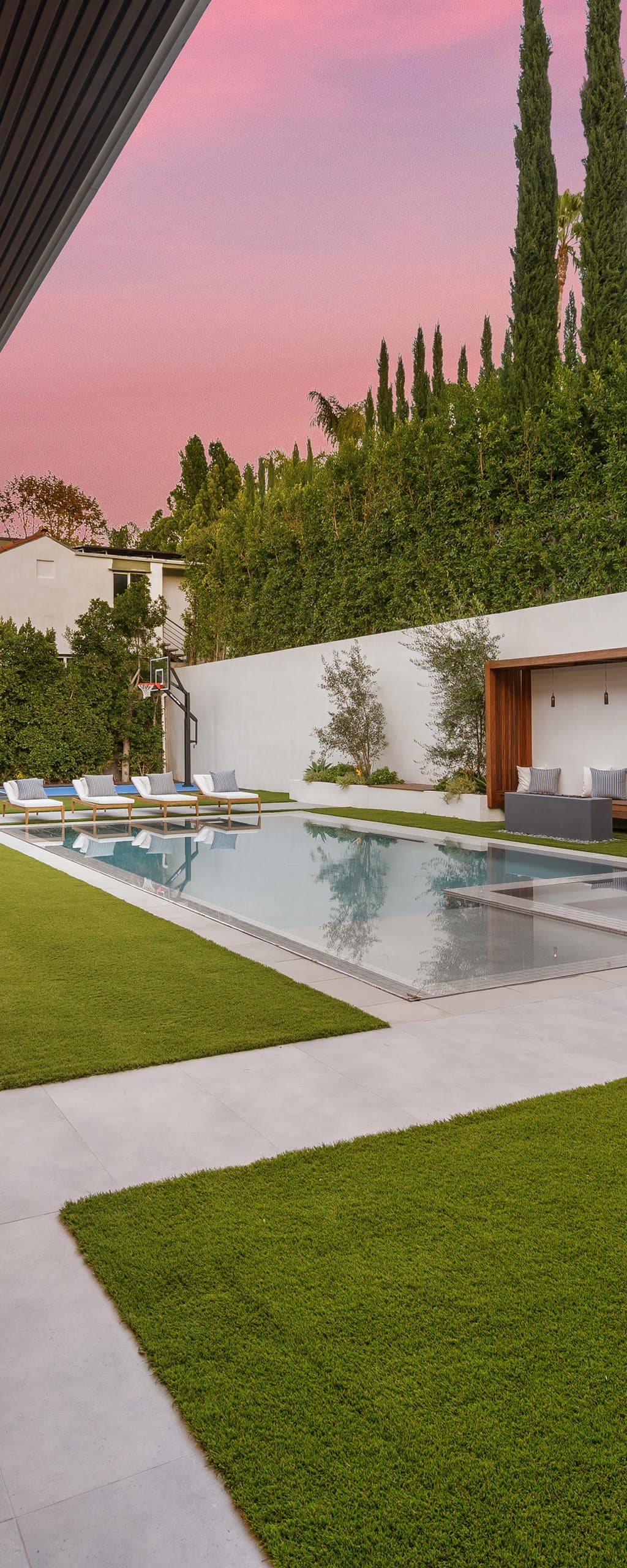 Oversized concrete slabs with turf joints leading to a modern pool house in the evening