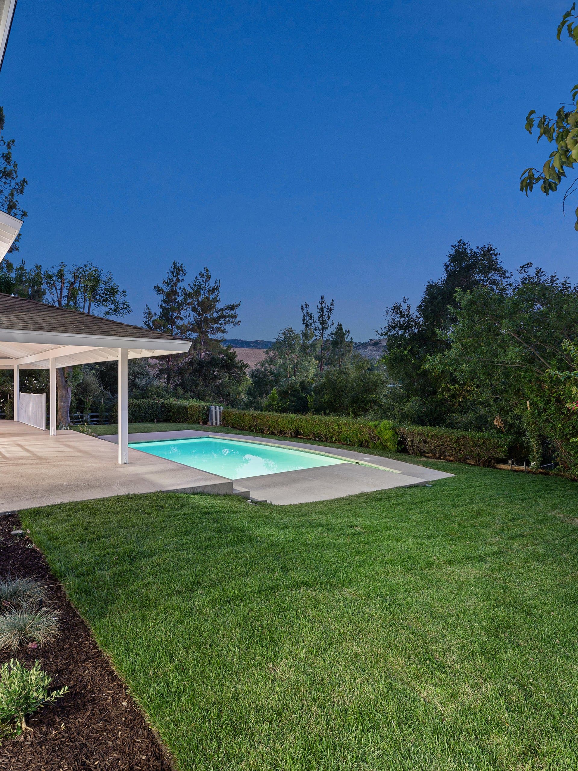 White patio home with pool and sod lawn at dusk
