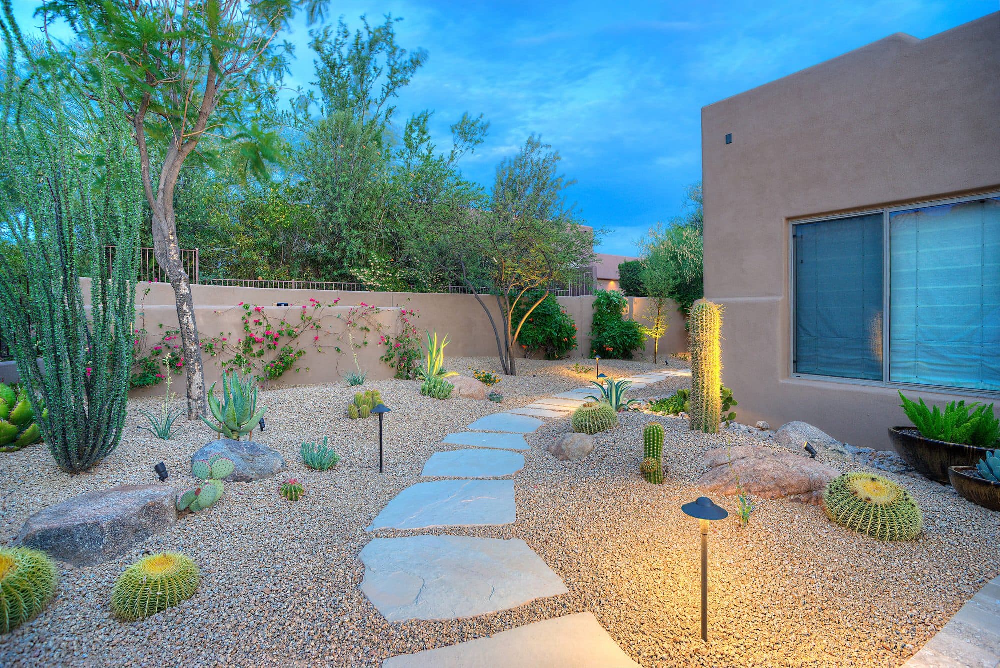 Zeroscape front yard at night with stucco walls, gravel, and accent lighting