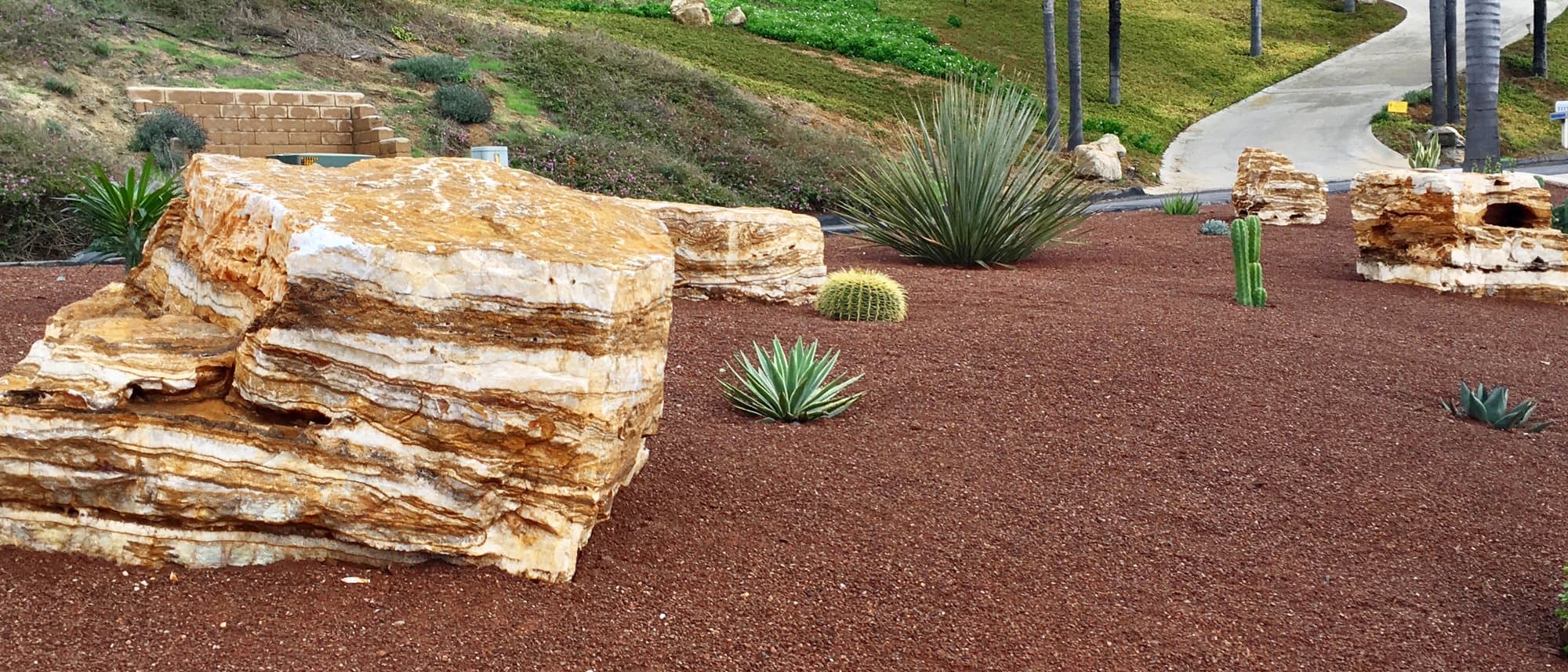 Layered sandstone boulders with red decomposed granite, agave, and cacti